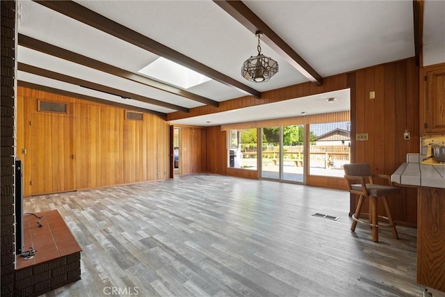living room with wooden walls, visible vents, and beam ceiling