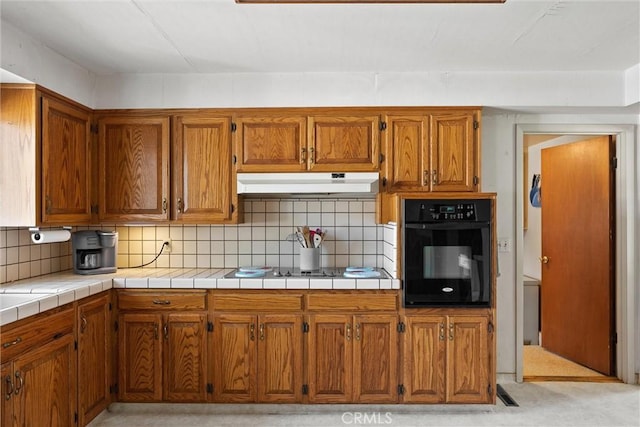 kitchen with decorative backsplash, under cabinet range hood, brown cabinets, and black appliances