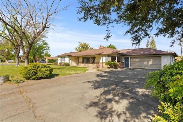 ranch-style house with an attached garage, a chimney, a front yard, and aphalt driveway