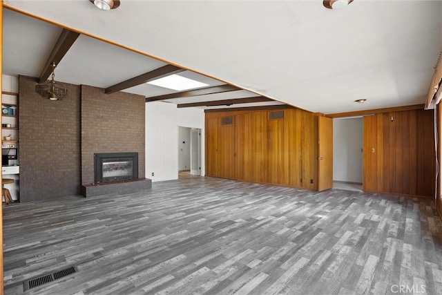 unfurnished living room with beamed ceiling, wooden walls, wood finished floors, and visible vents