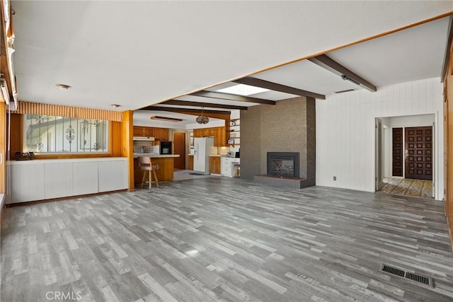 unfurnished living room featuring beamed ceiling, wood finished floors, visible vents, and a fireplace
