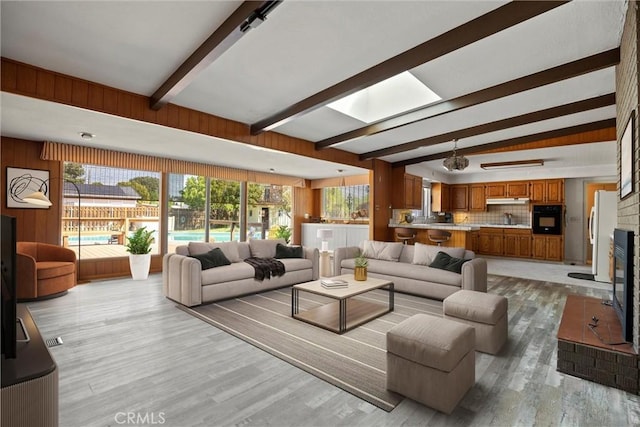 living room featuring light wood finished floors, a brick fireplace, and beam ceiling