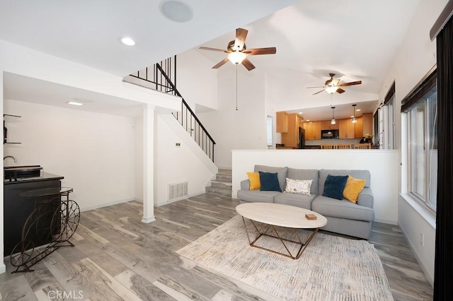 living area featuring high vaulted ceiling, a ceiling fan, stairs, visible vents, and wood finished floors