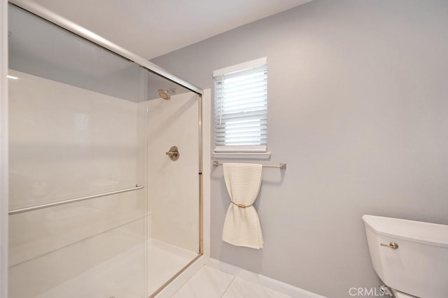 bathroom featuring toilet, tile patterned flooring, a shower stall, and baseboards