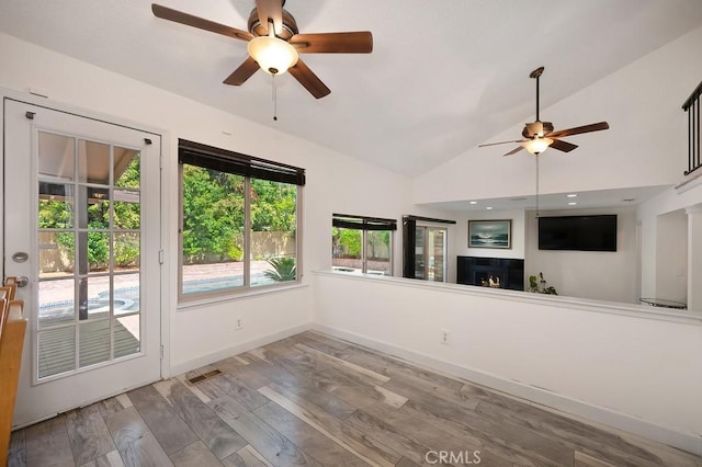 unfurnished living room featuring ceiling fan, wood finished floors, a lit fireplace, baseboards, and lofted ceiling