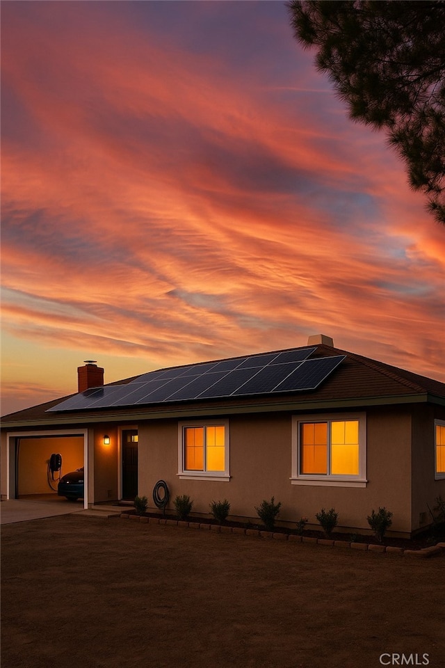 view of front of home with roof mounted solar panels, a chimney, concrete driveway, and stucco siding