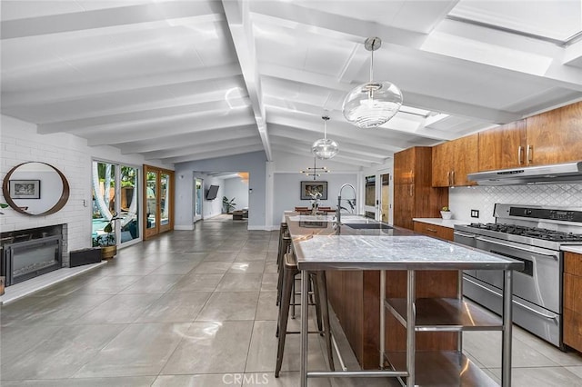kitchen featuring brown cabinets, a sink, under cabinet range hood, open floor plan, and stainless steel gas range oven
