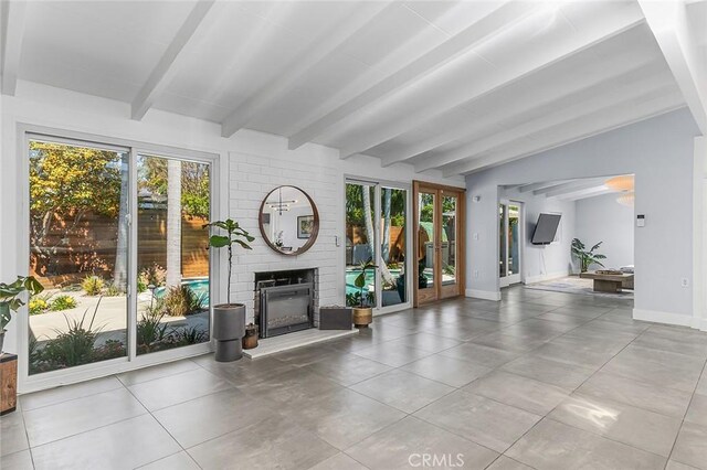 unfurnished living room with lofted ceiling with beams, a brick fireplace, tile patterned floors, and baseboards