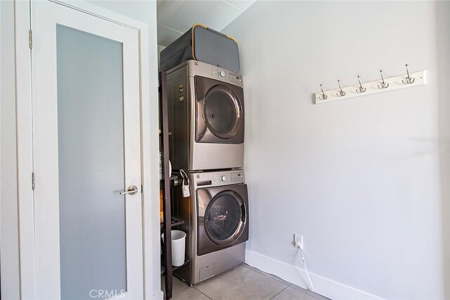 laundry room with light tile patterned floors, stacked washing maching and dryer, laundry area, and baseboards