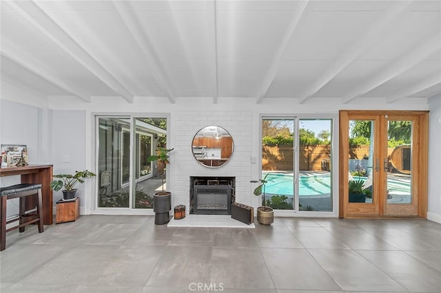 living area featuring beam ceiling, a wealth of natural light, and a brick fireplace