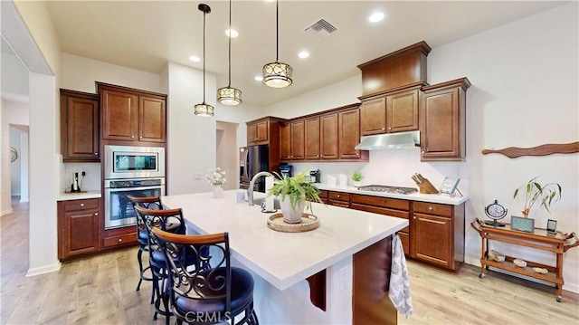 kitchen featuring light countertops, stainless steel appliances, under cabinet range hood, light wood finished floors, and visible vents