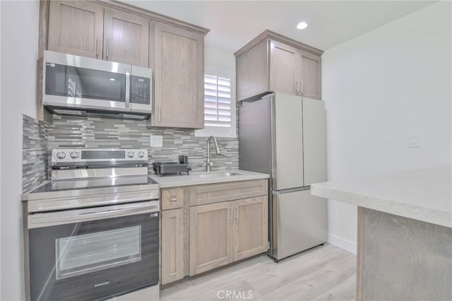 kitchen with backsplash, a sink, baseboards, light wood finished floors, and stainless steel appliances