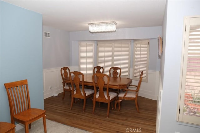 dining room with a decorative wall, wood finished floors, visible vents, and a wainscoted wall