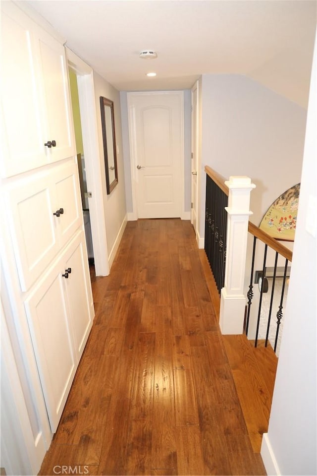 hallway featuring dark wood finished floors, baseboards, and an upstairs landing