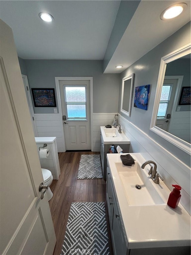 full bath with two vanities, wood finished floors, wainscoting, and a sink