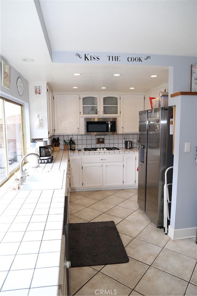 kitchen featuring a sink, backsplash, white cabinetry, tile countertops, and appliances with stainless steel finishes