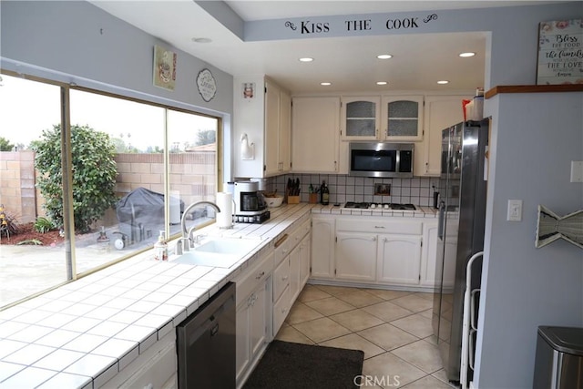 kitchen with tile countertops, dishwashing machine, a sink, and stainless steel microwave