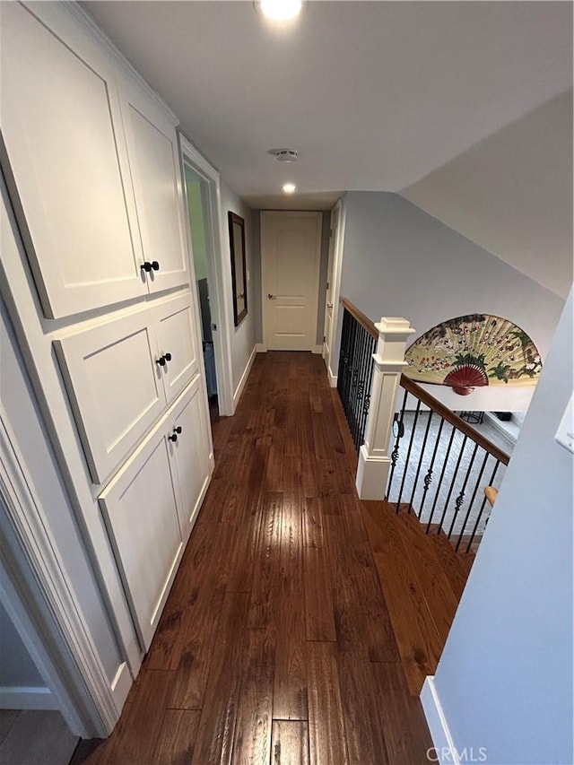hallway with vaulted ceiling, dark wood-style floors, and an upstairs landing