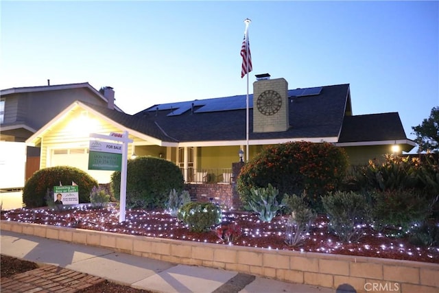 view of front of home with an attached garage, a chimney, and solar panels