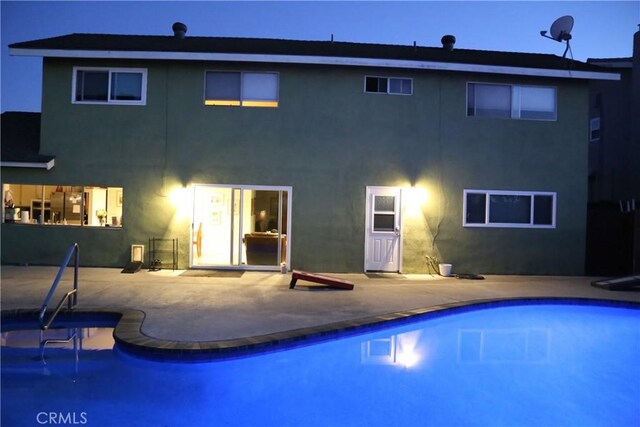 rear view of property with an outdoor pool, a patio, and stucco siding