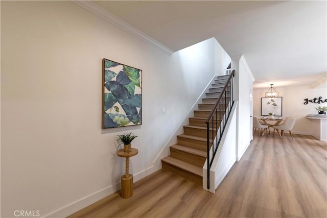 staircase featuring crown molding, baseboards, a chandelier, and wood finished floors