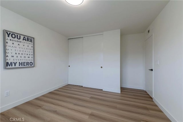 unfurnished bedroom with a closet, baseboards, and light wood-style floors