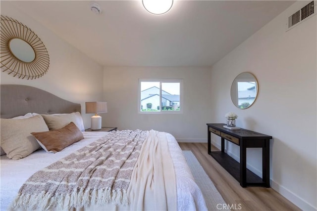 bedroom featuring baseboards, visible vents, vaulted ceiling, and wood finished floors
