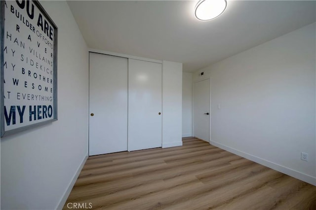 unfurnished bedroom featuring baseboards, light wood-type flooring, and a closet