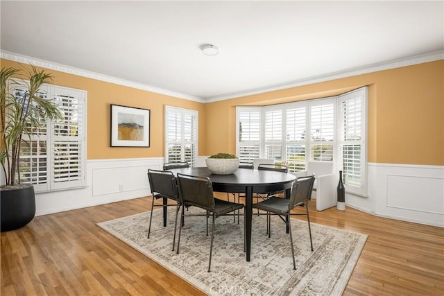 dining room with a wainscoted wall, ornamental molding, and wood finished floors