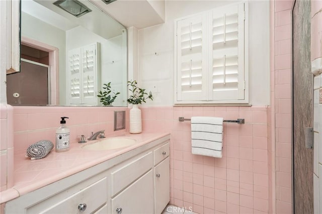 full bath featuring tile walls, a stall shower, vanity, and wainscoting