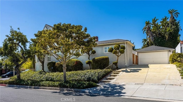 view of property hidden behind natural elements featuring an outdoor structure, stucco siding, concrete driveway, and a garage