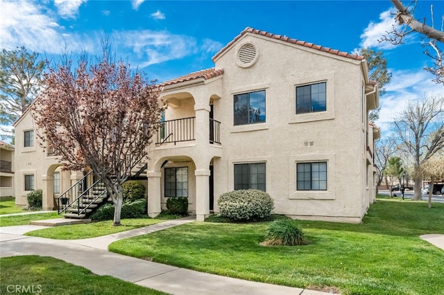 view of front of house featuring a tile roof, a balcony, a front lawn, stucco siding, and stairs