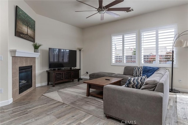 living area with visible vents, light wood finished floors, baseboards, ceiling fan, and a tiled fireplace