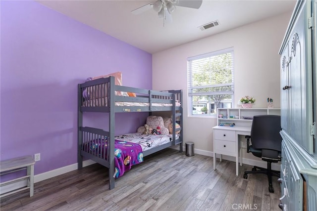 bedroom with a ceiling fan, visible vents, baseboards, and wood finished floors