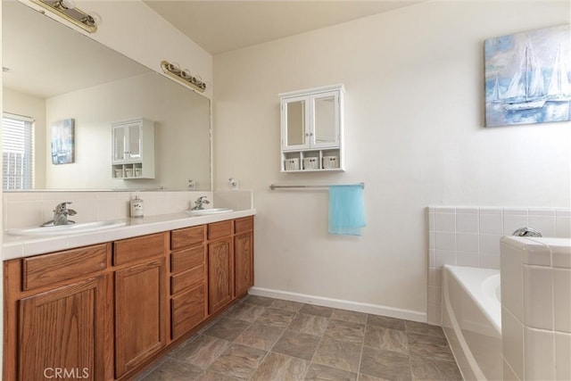 bathroom with a bath, double vanity, a sink, and baseboards