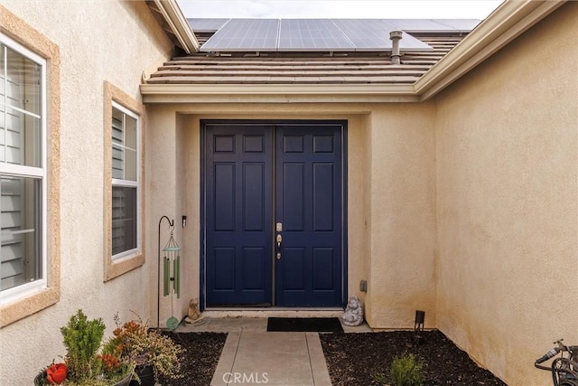 property entrance featuring roof mounted solar panels and stucco siding