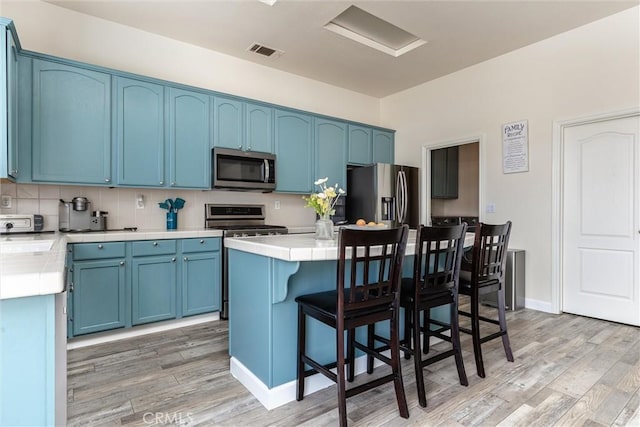 kitchen with visible vents, blue cabinetry, stainless steel appliances, light wood-style floors, and a kitchen breakfast bar