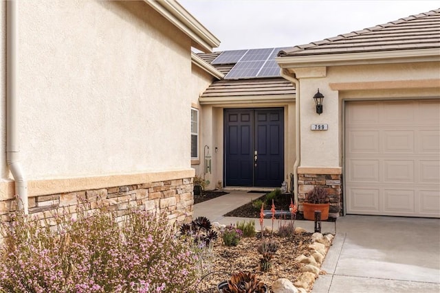 view of exterior entry featuring stone siding, a tiled roof, roof mounted solar panels, stucco siding, and driveway