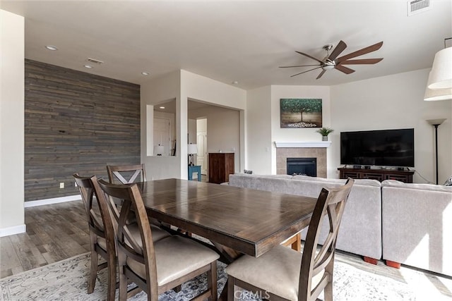 dining space featuring an accent wall, wood finished floors, wood walls, visible vents, and ceiling fan