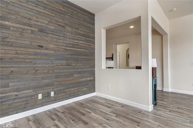 spare room with baseboards, wood finished floors, an accent wall, and wood walls