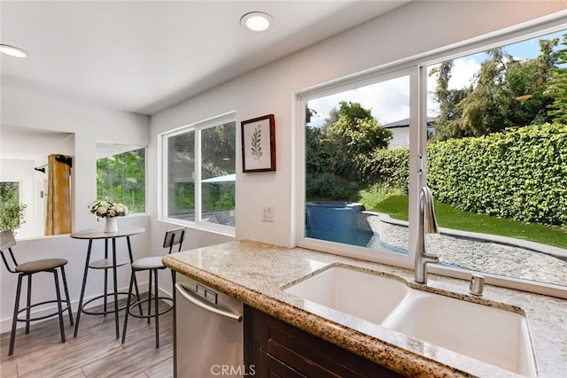 kitchen featuring stainless steel dishwasher, a sink, healthy amount of natural light, light stone counters, and recessed lighting