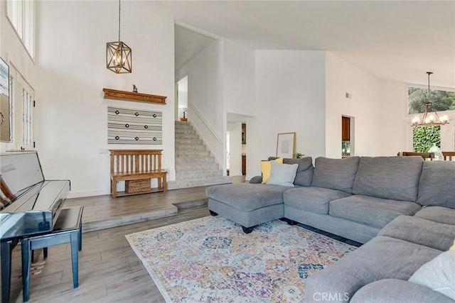 living room with a chandelier, high vaulted ceiling, wood finished floors, stairs, and baseboards