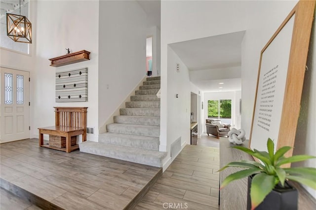 foyer with a towering ceiling, stairway, wood finished floors, and a chandelier