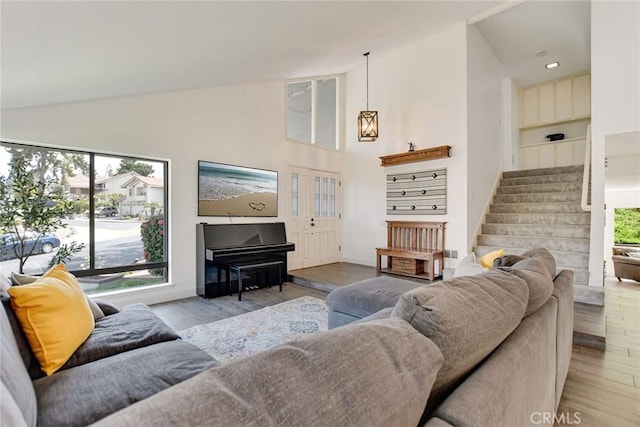 living room with wood finished floors, stairway, high vaulted ceiling, and baseboards