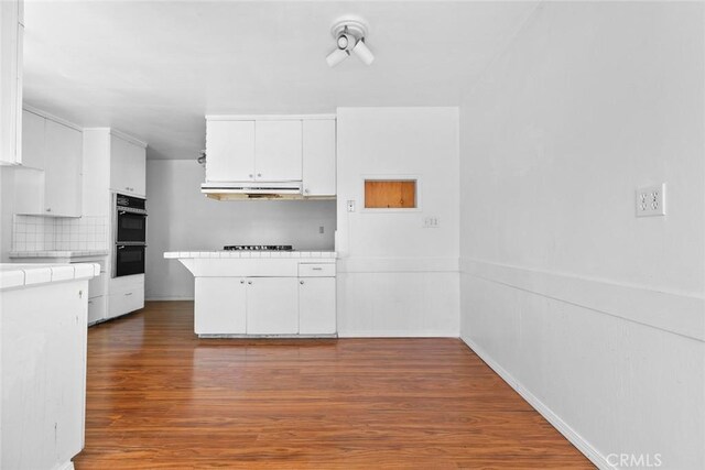 21032 Baltar St, Canoga Park, CA 91304 - kitchen with white cabinets, wood finished floors, under cabinet range hood, tile countertops, and black appliances
