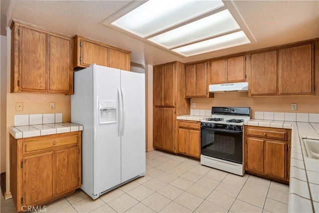 14935 Elizabeth Lake Rd, Lake Elizabeth, CA 93532 - kitchen featuring under cabinet range hood, brown cabinetry, range with gas cooktop, and white fridge with ice dispenser