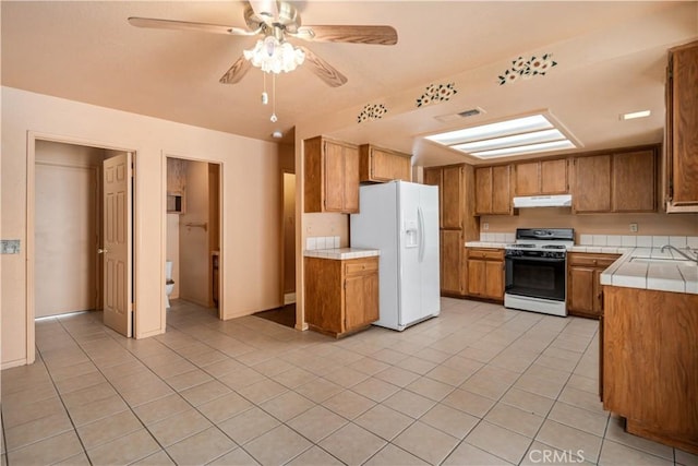 14935 Elizabeth Lake Rd, Lake Elizabeth, CA 93532 - kitchen with a ceiling fan, tile counters, white fridge with ice dispenser, under cabinet range hood, and range with gas stovetop