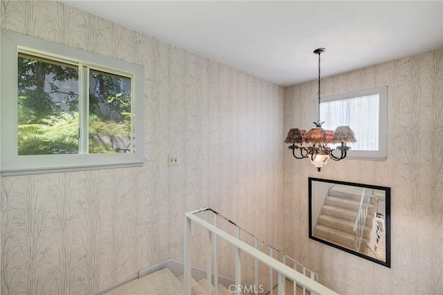 stairway featuring an inviting chandelier and wallpapered walls