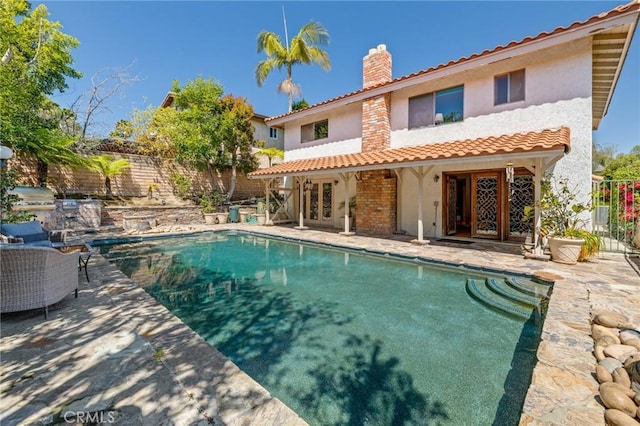 rear view of house with french doors, a fenced backyard, a chimney, and stucco siding