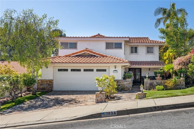 mediterranean / spanish-style house with driveway, stucco siding, an attached garage, and a tile roof